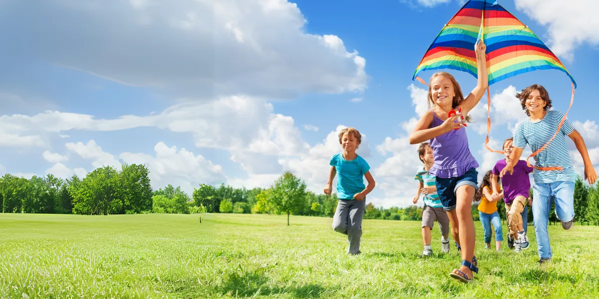 Group of kids flying a kite while running through a field